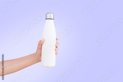 Hand holding white steel bottle on background of very peri color. Close-up view. photo