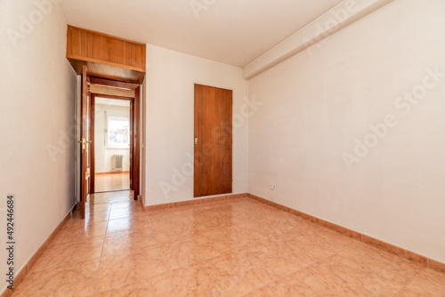 empty room with orange stoneware floor  mahogany wood door and white painted walls and brass door handle on built in wardrobe and trunk