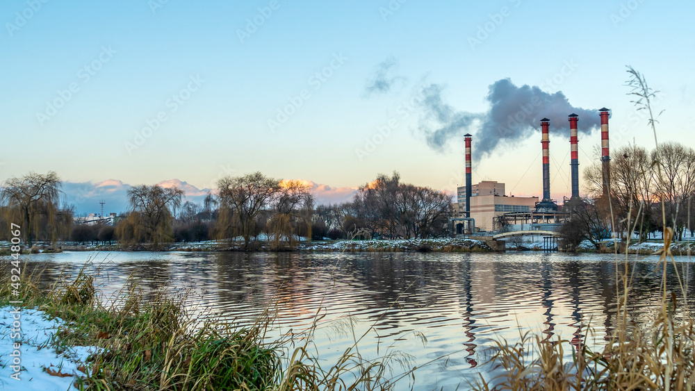 Power station with reservoir in winter. Beautiful seaside winter sunset with a smoking factory chimney.