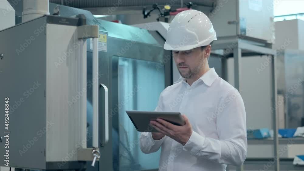 An engineer at an industrial plant. A worker controls the operation of a CNC milling machine. Tablet computer in hand. Drill manufacturing plant. An engineer at an industrial plant. A worker controls the operation of a CNC milling machine. Tablet computer in hand. Drill manufacturing plant.