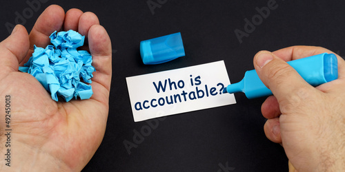 In the hands of crumpled paper, a marker, next to a business card with the inscription - Who is accountable photo