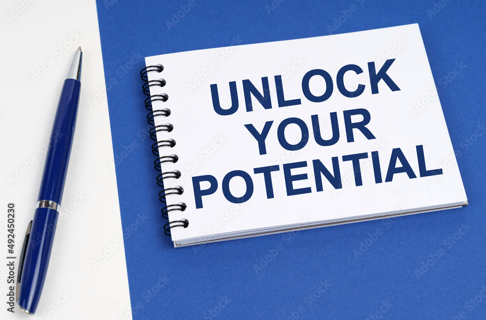 On a blue-white surface lies a pen and a notebook with the inscription - Unlock Your Potential On a blue-white surface lies a pen and a notebook with the inscription - Unlock Your Potential