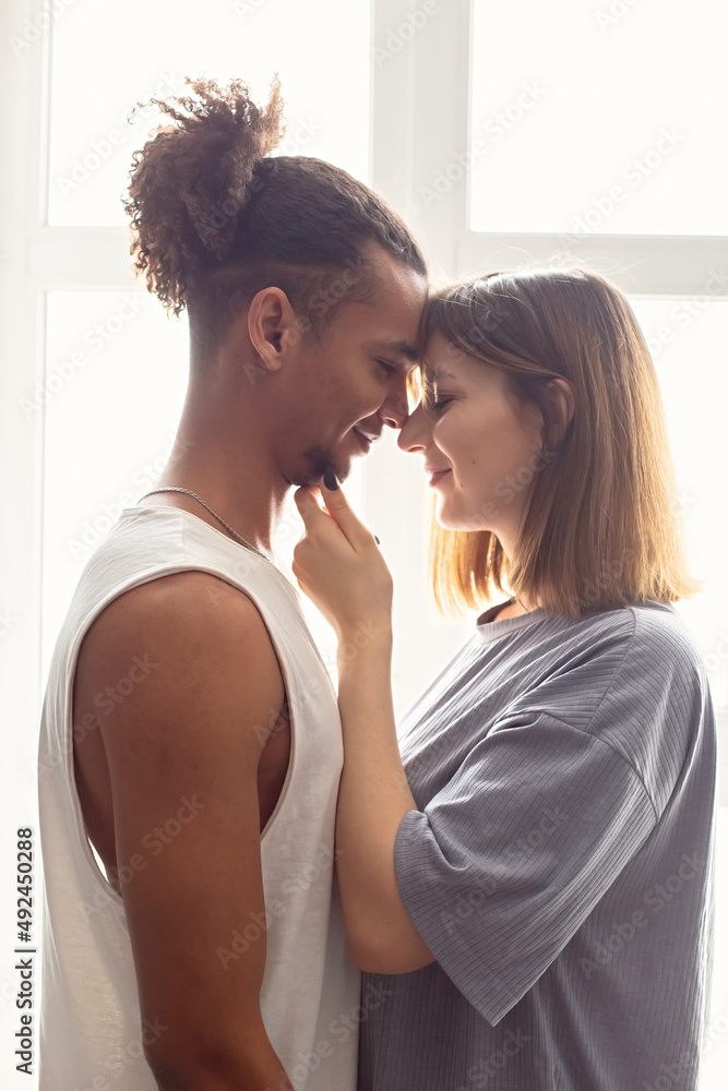 Naklejka premium Portrait of a multiracial couple, boyfriend and girlfriend face to face, stand near the window