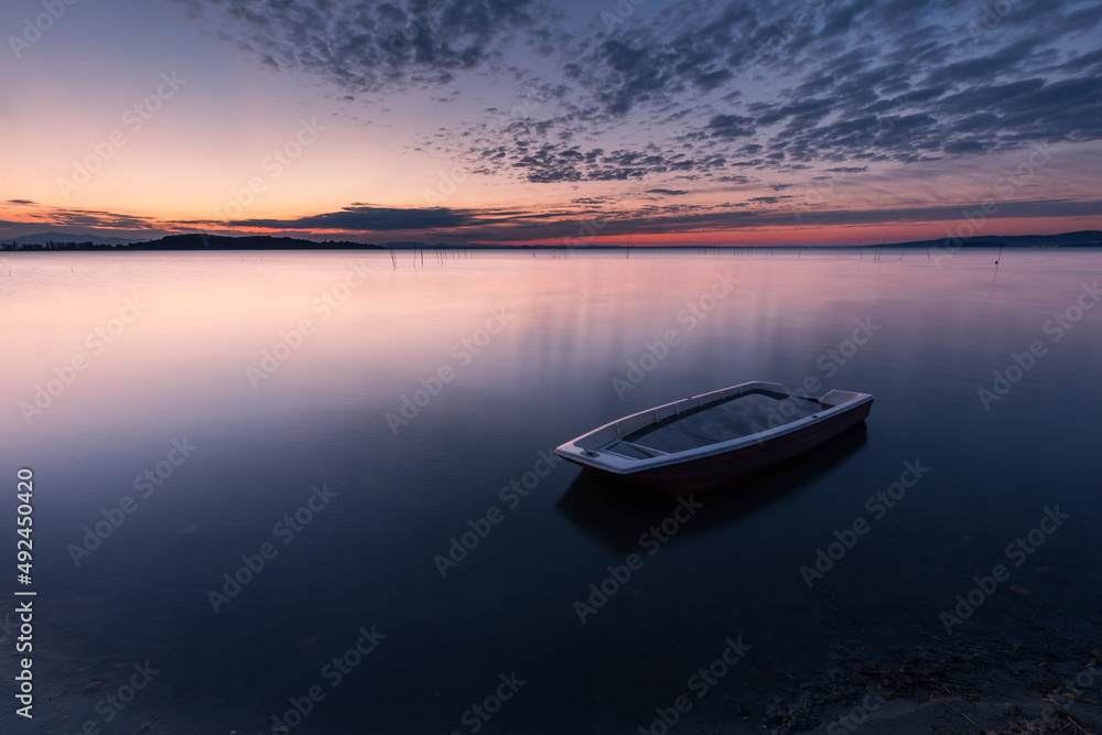 Surreal long exposure view of shore of Trasimeno lake Umbria, Italy with a little boat and perfectly still water