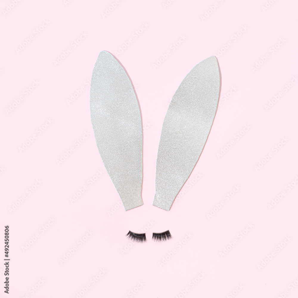 Easter bunny ears with lashes on a pastel pink background. Futuristic aesthetic surreal Easter concept.