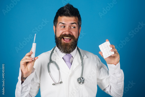 Bearded doctor with pills and syringe in hands. Smiling physician with stethoscope and medical gown. photo