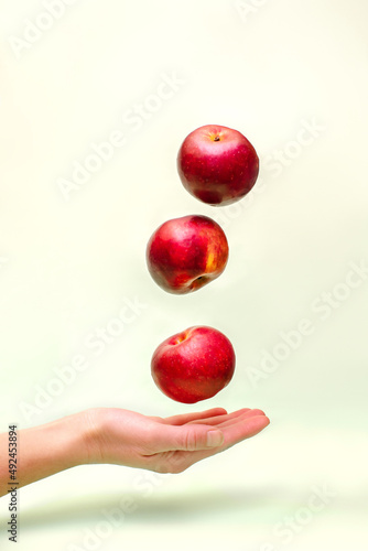 Flying levitating floating red ripe fresh juicy apples in air above female womens hand on green background. Levity summer fruits. Trendy, minimal Creative food