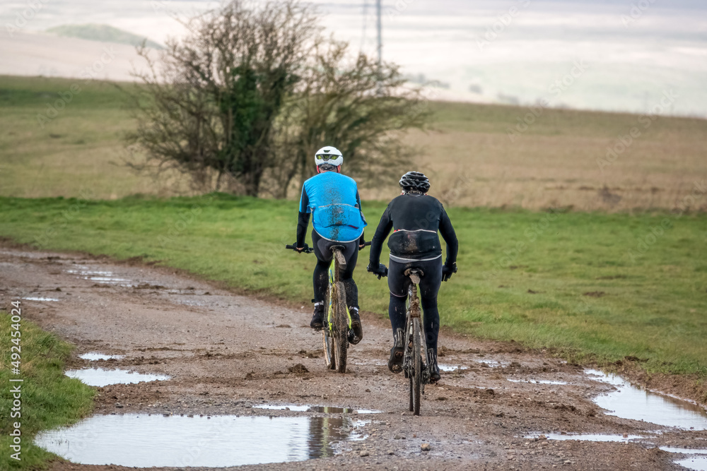 a pair of casual cyclists on a muddy stone track crossing salisbury plain, Wiltshire UK