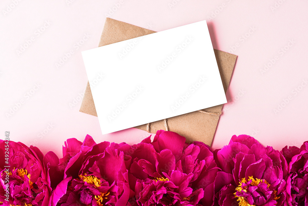 Blank greeting card with pink peony flowers on pink background. Wedding invitation. Mock up. Flat lay
