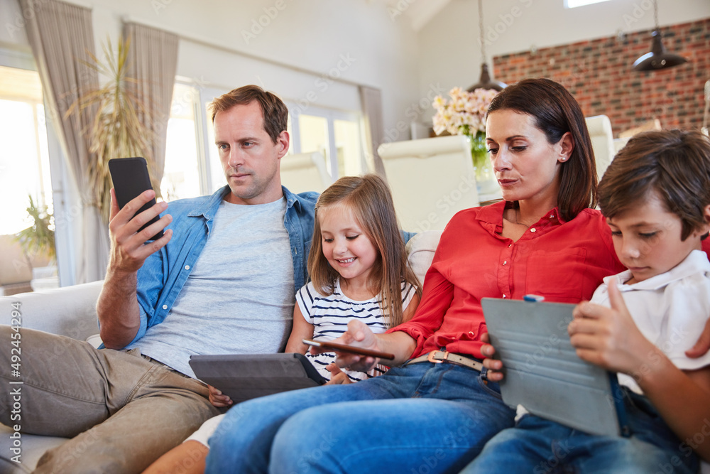 Digital distractions. Shot of a young family sitting together on their living room sofa distracted by various media and devices.