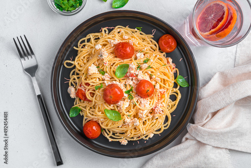 Spaghetti with baked feta, cherry tomatoes, herbs and basil on a gray background.