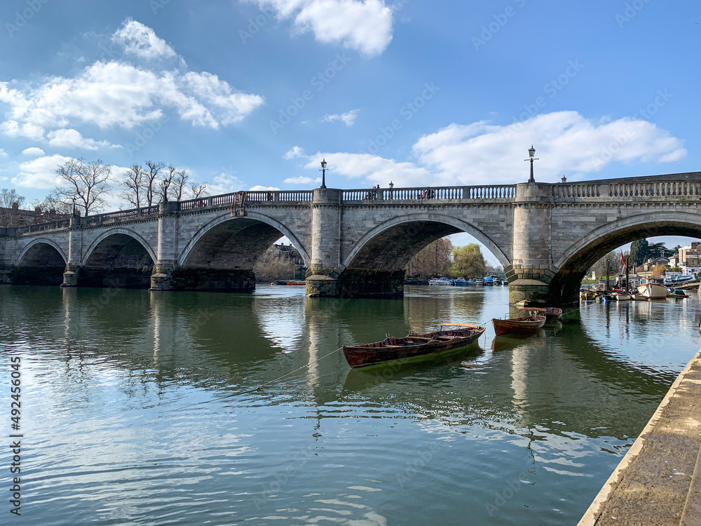 Richmond bridge is oldest bridge in capital. Moored vessel boats at Richmond Bridge Boat Club at the Thames riverside, south west London. Richmond Bridge is on the background
