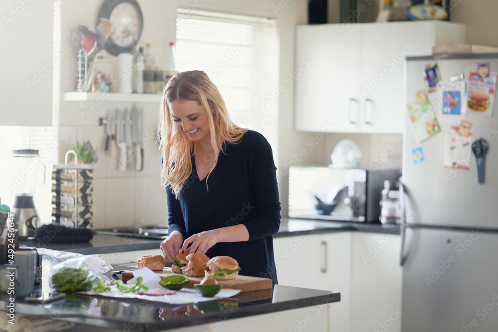 Burgers packed with the goodness of fresh ingredients. Shot of an attractive young woman preparing a meal at home.