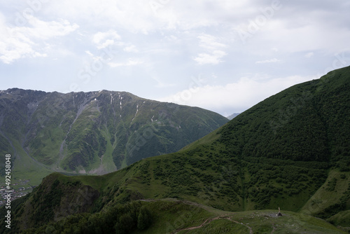 the Kazbegi mountain ranges in Georgia are green and have a clear sky above them.