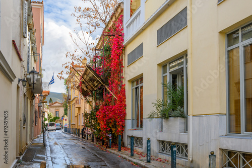 Fototapeta Naklejka Na Ścianę i Meble -  An empty street in the Plaka area of Athens, Greece after a morning rain with colorful foliage covered a wall in Autumn.