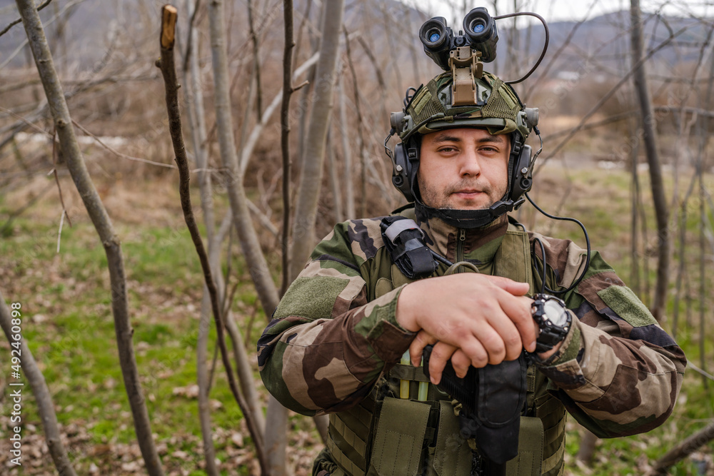 one man front view portrait of soldier in camouflage uniform armed with rifle ready to go on a mission in war zone standing outdoor in nature looking to the camera dogs of war mercenaries or volunteer