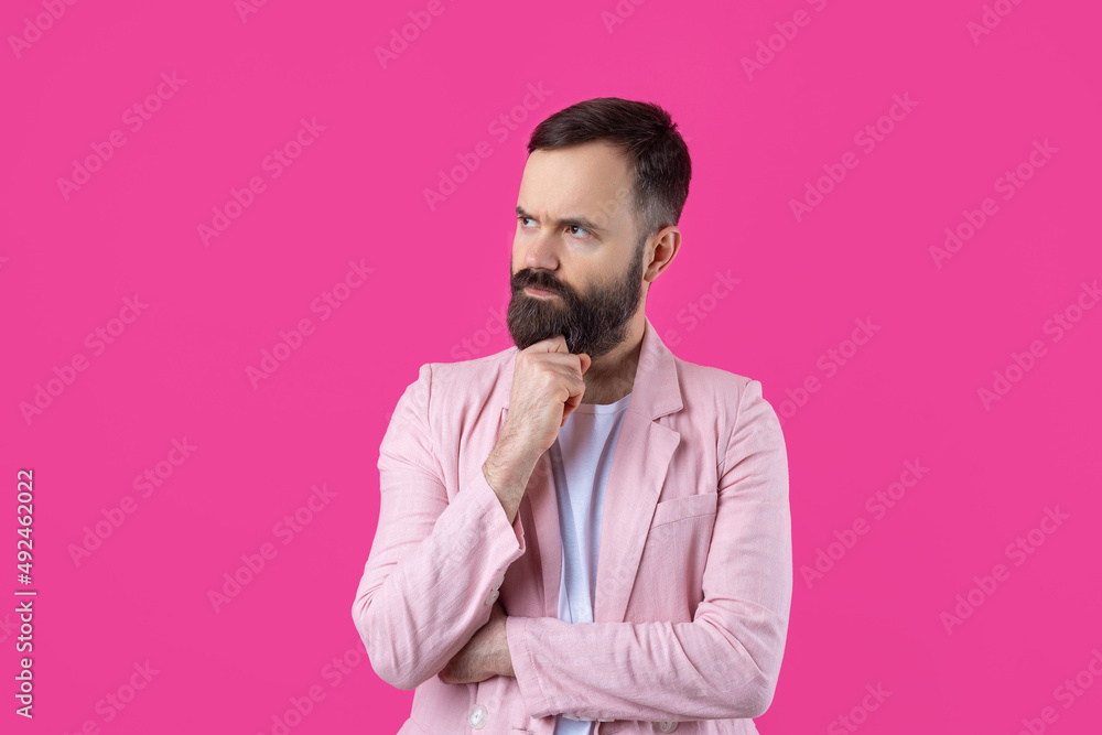 Handsome man with a beard in a pink jacket is thinking over an isolated red background.
