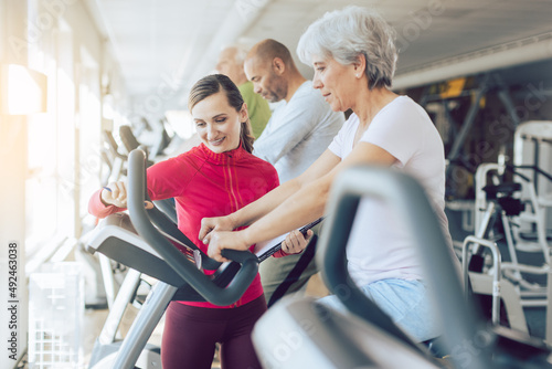 Fitness coach in gym helping senior people during cardio bike training