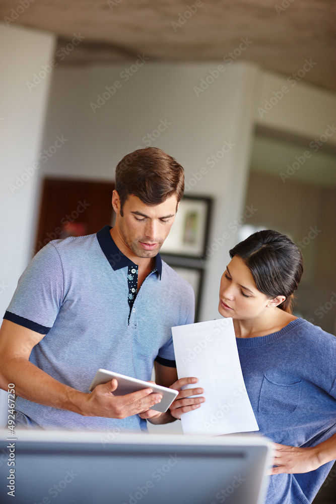 The benefits of teamwork. Cropped shot of a man using a digital tablet while his wife stands by with a document. The benefits of teamwork. Cropped shot of a man using a digital tablet while his wife stands by with a document.