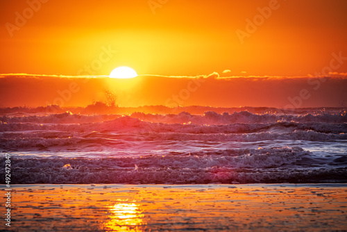 A setting sun reflects off of ocean waves creating a colorful sunset sky