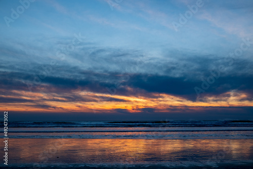 A beach with reflective sand at sunset  clouds streaking across the sky