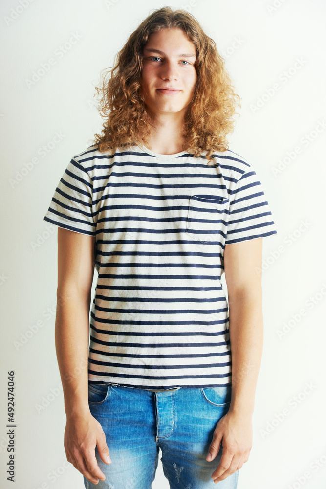 Unique and stylish. Young man with curly long hair standing by himself. Unique and stylish. Young man with curly long hair standing by himself.