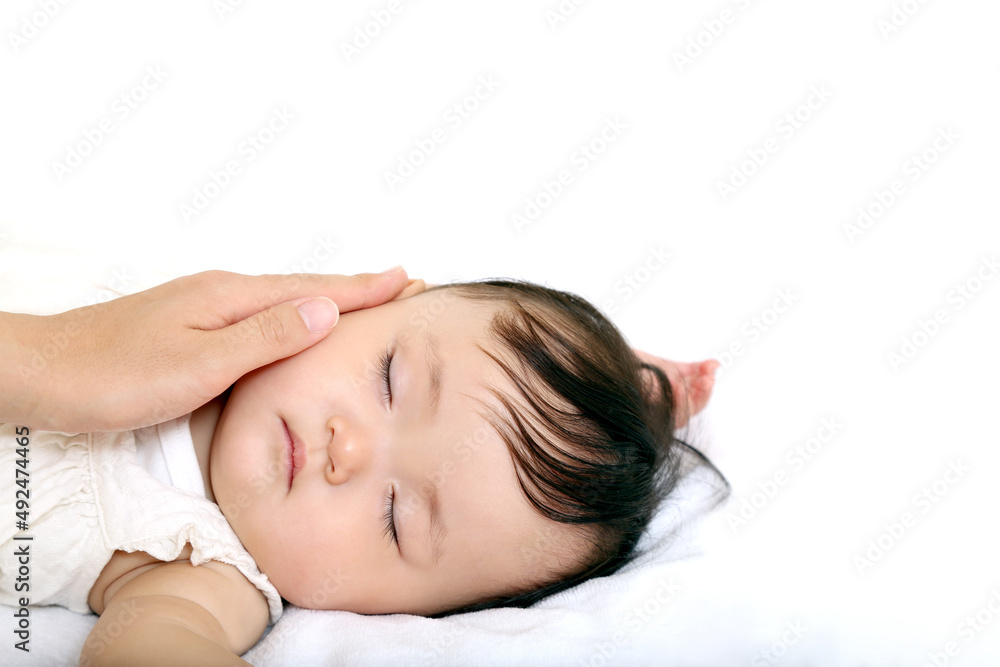 白背景で寝ている女の子の赤ちゃんの頬を撫でる母の手。愛情,家族,母性のイメージ