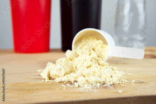 Whey protein powder in scoop with vitamins and plastic shaker on wooden background.
