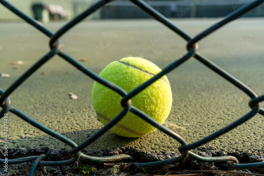 Close up of tennis ball behind the wires on the court