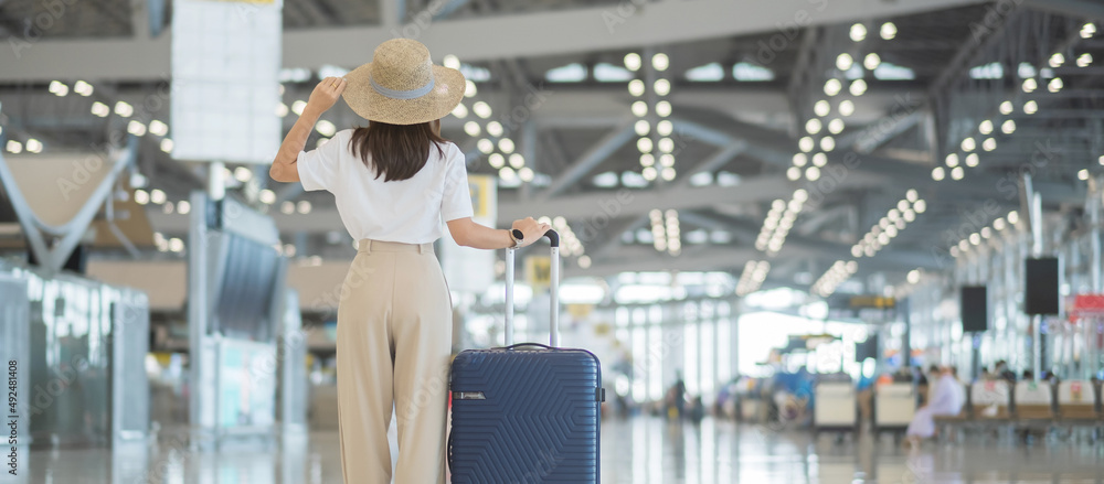 Young woman hand holding luggage handle before checking flight time in airport, Transport, insurance, travel and vacation concepts - obrazy, fototapety, plakaty 