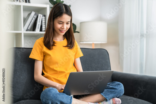 Young cheerful woman sitting on sofa and using laptop computer at home.
