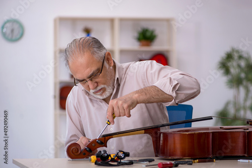Fotografie Old male repairman repairing musical instruments at workshop