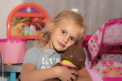 little blond girl playing, and holding a black doll