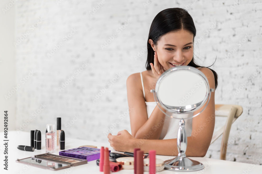 Smiling of young beautiful pretty woman clean fresh healthy white skin looking at mirror.girl touching on her face with hand and applying cream at home.spa and beauty concept Smiling of young beautiful pretty woman clean fresh healthy white skin looking at mirror.girl touching on her face with hand and applying cream at home.spa and beauty concept