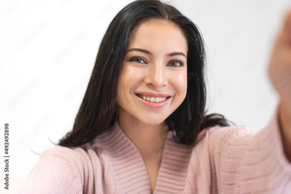 Portrait of smiling cheerful beautiful pretty asian woman clean fresh healthy white skin posing smile look at camera making live selfie on smartphone on the bed at home Portrait of smiling cheerful beautiful pretty asian woman clean fresh healthy white skin posing smile look at camera making live selfie on smartphone on the bed at home