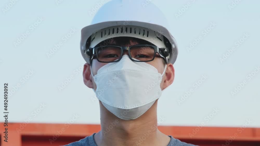 Young Asian engineer wearing a helmet and mask looks and smiles at the camera on the dam background. A young engineer works in a dam during the coronavirus outbreak. Young Asian engineer wearing a helmet and mask looks and smiles at the camera on the dam background. A young engineer works in a dam during the coronavirus outbreak.