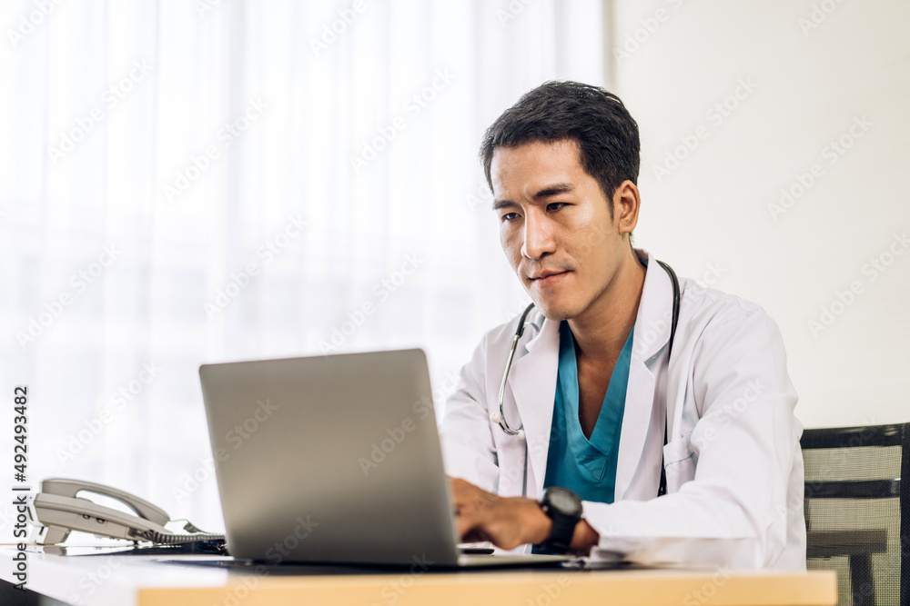 Asian man doctor wearing uniform with stethoscope working with laptop computer in hospital.healthcare and medicine Asian man doctor wearing uniform with stethoscope working with laptop computer in hospital.healthcare and medicine