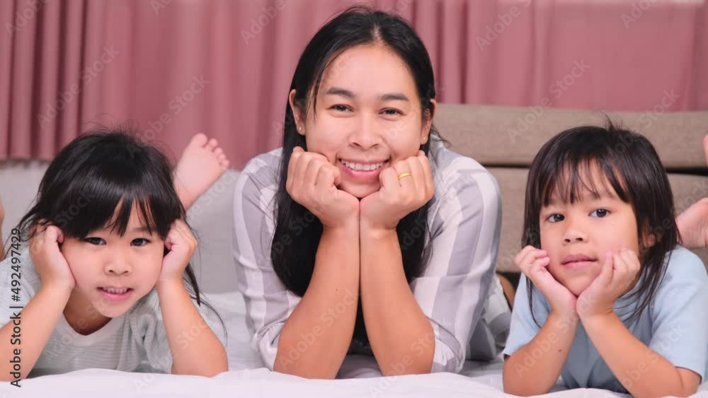Two tender daughters kissing happy mother. Happy children playing with their mother lying on a bed at home and  looking at the camera.