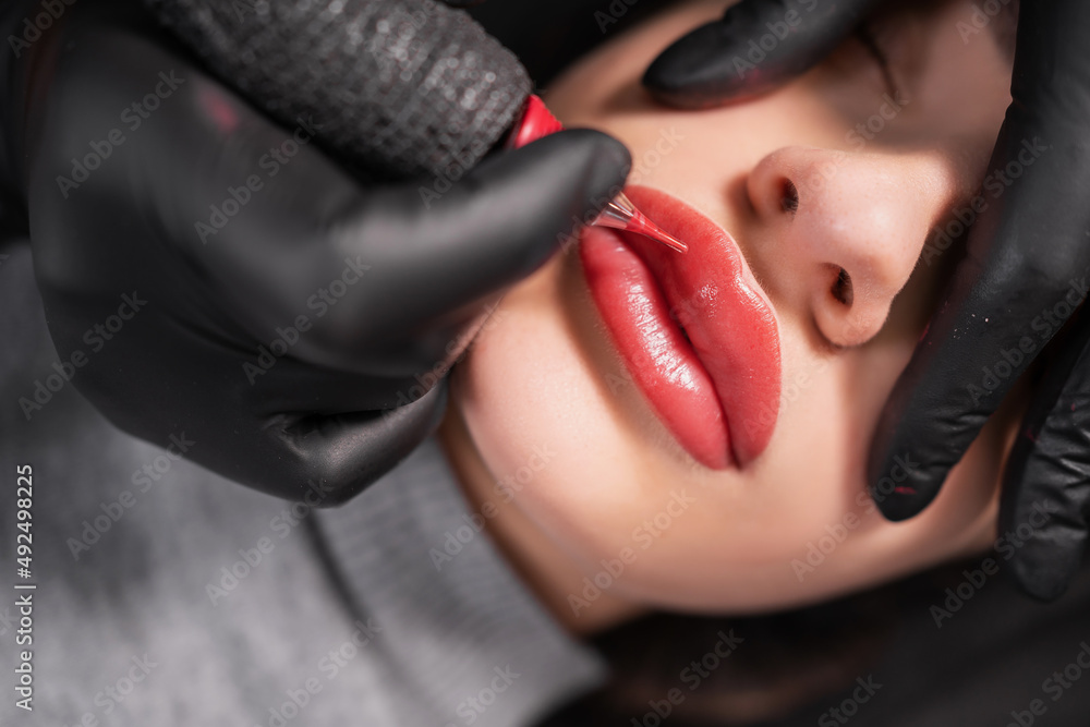 Close-up of swollen female lips during the application of permanent makeup. Tattoo on the face and micropigmentation of the lips. Professional facial microblading. - obrazy, fototapety, plakaty 