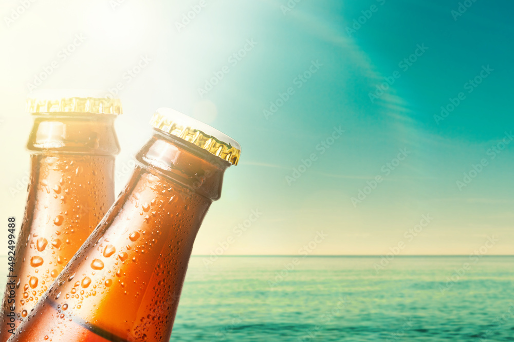 Close-up of the necks of two wet glass bottles of dark beer against the background of the ocean and the sky. Copy space. Alcoholic beverages on vacation