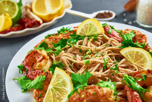 Stir fry noodle with shrimps, lemon and fresh parsley on white plate, soba with prawns, asian cuisine, top view