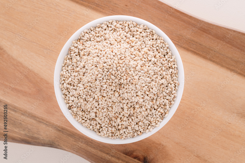 Sesame seeds in a white bowl on a wooden plate. Sesame seeds in a white bowl on a wooden plate.