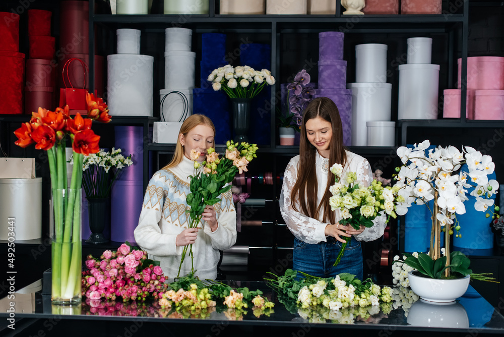 Two young women take orders by phone and make beautiful festive bouquets in a cozy flower shop. Floristry and bouquet making in a flower shop. Small business.