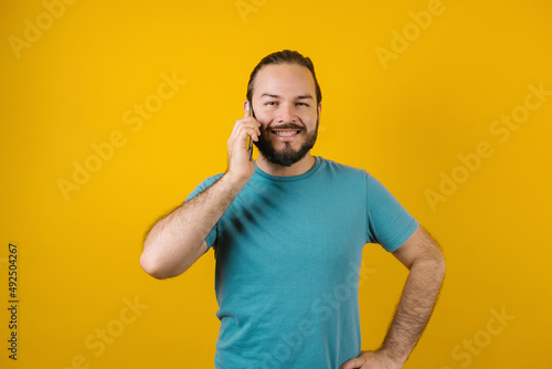 Young hispanic man using mobile phone in a phone call on yellow background in Mexico Latin America 