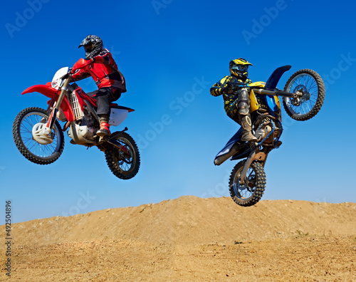 Extreme to the max. Action shot of two dirt bikers jumping in different directions.