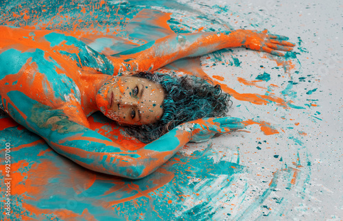 Head and upper body of expressive sexy naked woman lying elegant on the floor in turquoise blue orange color abstractly painted torso bodypainting woman on the splashed ground photo
