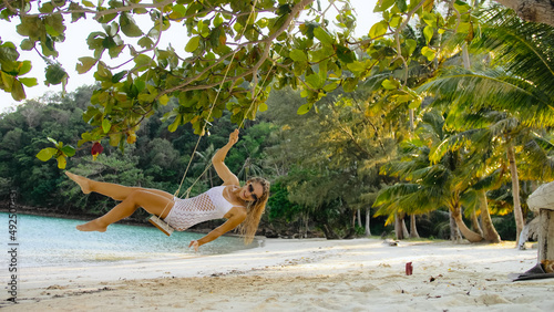 Radiant woman is swinging on a swing. Charming girl spends her vacation at the seaside. Concept natural beauty body health, sensuality, lifestyle alone travel, relaxation