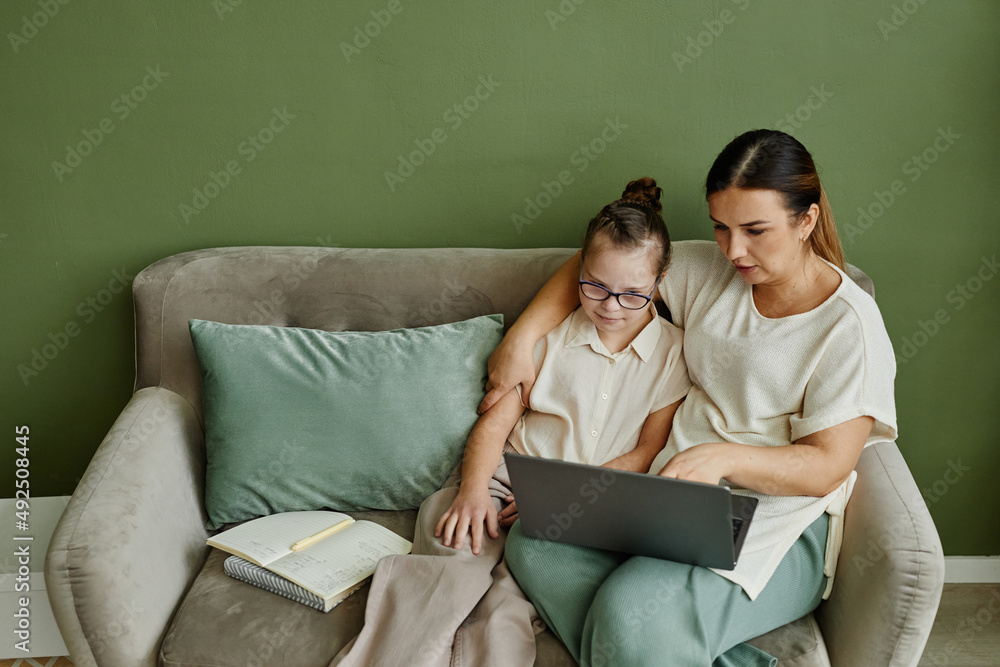 Minimal portrait of mother and daughter with down syndrome relaxing on couch together in cozy home, copy space Minimal portrait of mother and daughter with down syndrome relaxing on couch together in cozy home, copy space