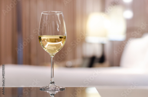 A glass of white wine puts on table in bed room. Relaxing at home concept.