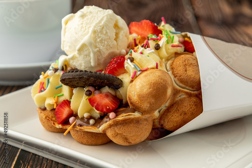 Hong kong or bubble waffle with ice cream, fruits, chocolate sauce and colorful candy photo